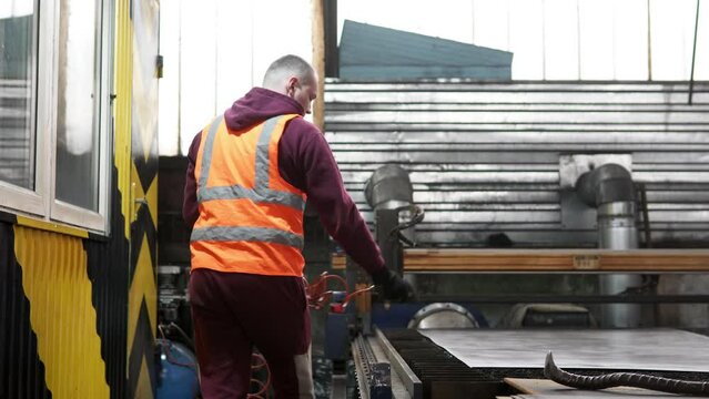 An operator of a CNC machine for plasma cutting of metal cleans the work surface after operating a plasma laser at a metallurgical plant. Manufacturing parts using a computer program.