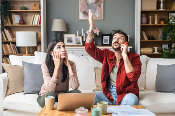 Young frustrated and annoyed couple working from home calling the police or neighbor to turn down...