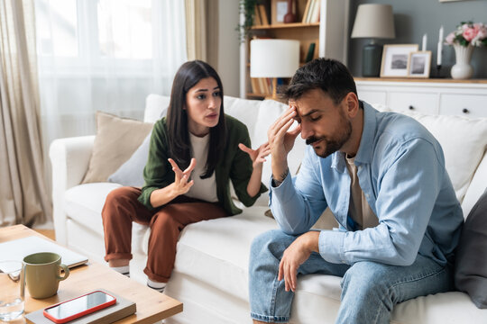 Communication problems, relationship difficulties. Young couple man and woman sitting on sofa at home, argue and misunderstanding. Two angry and sad people having issue with ego and guilt.