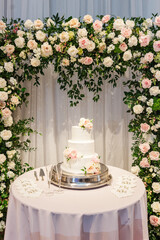Vertical shot of a wedding cake on a table by a floral archway