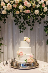 Vertical shot of a wedding cake on a table by a floral archway