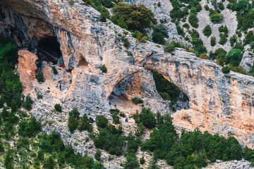 A group of people are climbing a rocky mountain. The mountain has a large cave. They are in...