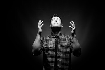 Black and white photo of a man looking up with open hands in surrender.
