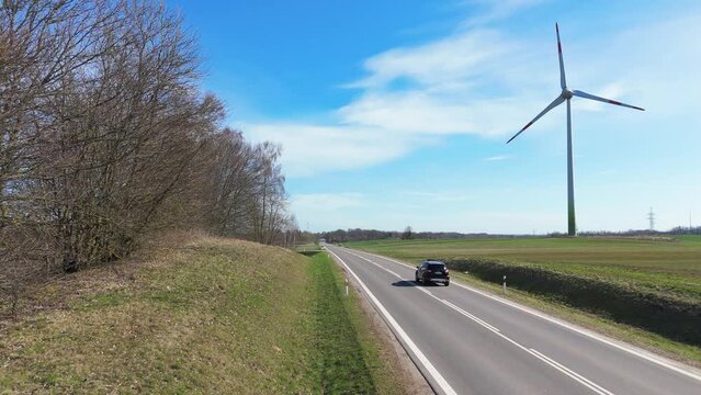 Car driving on a paved road passing through green fields with wind turbines in Taurage, Lithuania