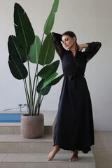 Beautiful brunette woman portrait smile. Portrait of young pretty woman in black night gown in her bathroom. Closeup, big lips. Plants, wooden table.
