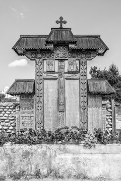 Densus village, Hunedoara county, Transylvania, Romania: Traditional carved wooden cross with the Crucifixion scene at the entrance to the Densuș Church and yard in  black and white