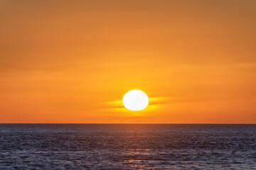 large yellow sun casts its reflection upon the sea's surface, bathing in the golden glow of sunrise