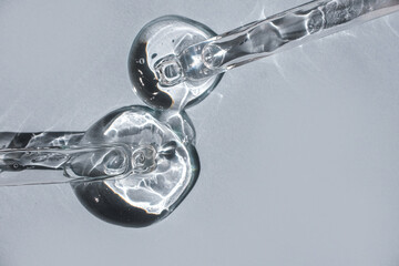 Cosmetic gel and two glass pipettes on a gray background.