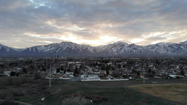 Drone view of a small city in front of the snowy Wasatch Range at sunset time in America