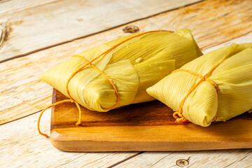 Traditional Brazilian pamonha made from corn wrapped in corn husks, presented on a wooden board,...