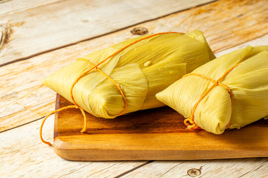 Traditional Brazilian pamonha made from corn wrapped in corn husks, presented on a wooden board, highlighting the rich texture and authentic look of the dish.