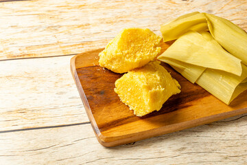 Traditional Brazilian pamonha served on a rustic wooden board. Delicious yellow cornmeal dish wrapped in corn husks.