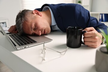 Man with cup of drink sleeping at table in office