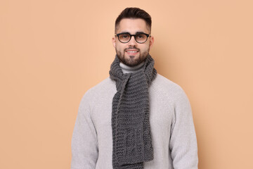 Fototapeta premium Smiling man in knitted scarf on beige background