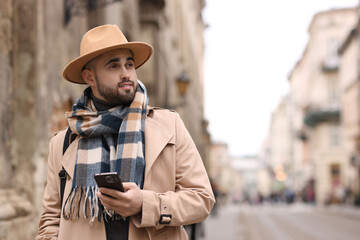 Handsome man in warm scarf with smartphone outdoors. Space for text