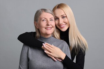 Family portrait of young woman and her mother on grey background