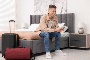 Smiling guest with smartphone on bed in stylish hotel room