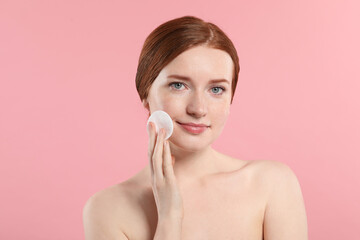 Beautiful woman with freckles wiping face on pink background