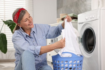 Happy housewife with laundry basket near washing machine at home