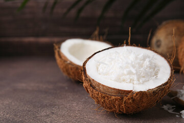 Coconut pieces in nut shell on brown table, space for text