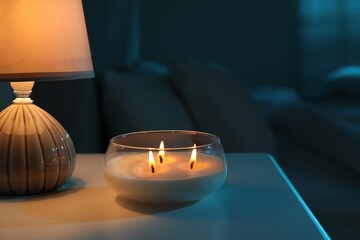 Burning scented candle and lamp on bedside table in bedroom at night