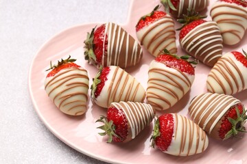 Heart shaped plate with delicious chocolate covered strawberries on light table, closeup