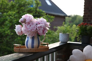 Beautiful pink peony flowers in vase on balcony railing outdoors