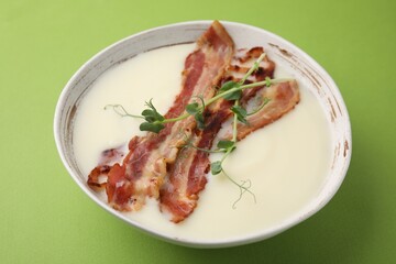 Delicious potato soup with bacon and microgreens on green background