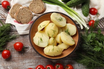 Young boiled potatoes with dill in bowl among products on wooden rustic table, flat lay