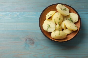 Young boiled potatoes with dill in bowl on light blue wooden table, top view. Space for text