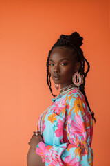 Fototapeta premium A pregnant Black woman in a colorful floral blouse and large earrings on orange background. Modern maternity fashion and vibrant style, perfect for content related to pregnancy, fashion, and wellness.
