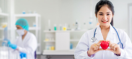 Smile beautiful young Asian doctor hold heart shape in hand standing at laboratory background 