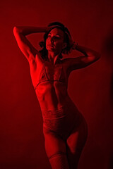 Portrait of a woman in lingerie under red lighting, showcasing her fit physique and serious expression.