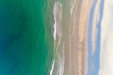 shore of a turquoise water beach at dawn as seen from a drone