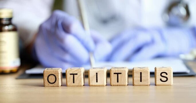 Text on cubes otitis media and doctor in background. Otitis symptoms and treatment in adults and children concept