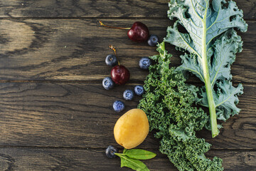 Leaves of green kale with blueberry and cherry on table with copy space