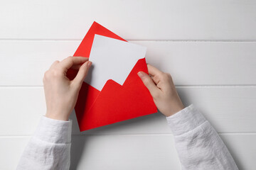 Woman taking card out of letter envelope at white wooden table, top view