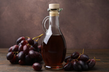 Jug with wine vinegar and grapes on wooden table, closeup