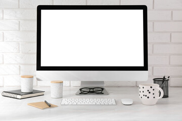 Fototapeta premium Office workplace with computer, cup and stationery on light table near white brick wall