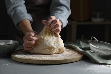 Woman kneading dough at grey table, closeup