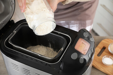 Making dough. Woman adding flour into breadmaker machine, closeup