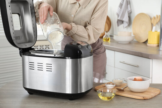 Making dough. Woman adding flour into breadmaker machine at wooden table, closeup