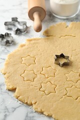 Making shortcrust pastry. Raw dough, rolling pin and cookie cutters on white marble table