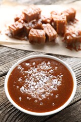 Caramel sauce with sea salt in bowl on wooden table, closeup