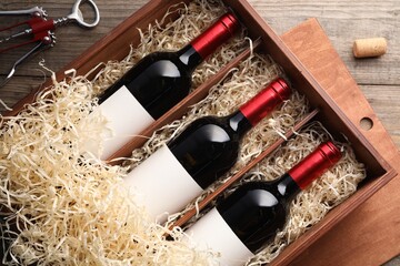 Box with wine bottles, corkscrew and cork on wooden table, flat lay