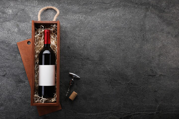 Bottle of wine in wooden box, cork and corkscrew on dark textured table, flat lay. Space for text