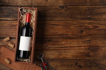 Box with wine bottle, corkscrew and corks on wooden table, flat lay. Space for text