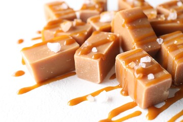 Tasty candies, caramel sauce and salt on white table, closeup