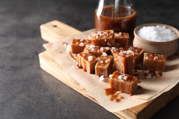 Tasty candies, caramel sauce and salt on grey table