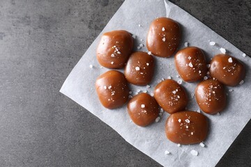 Tasty caramel candies and salt on grey table, top view. Space for text